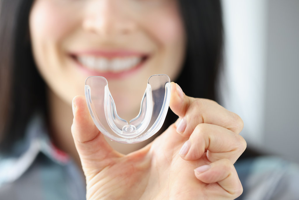Smiling woman holds transparent plastic mouth guard in her hand Airways and Orthodontics