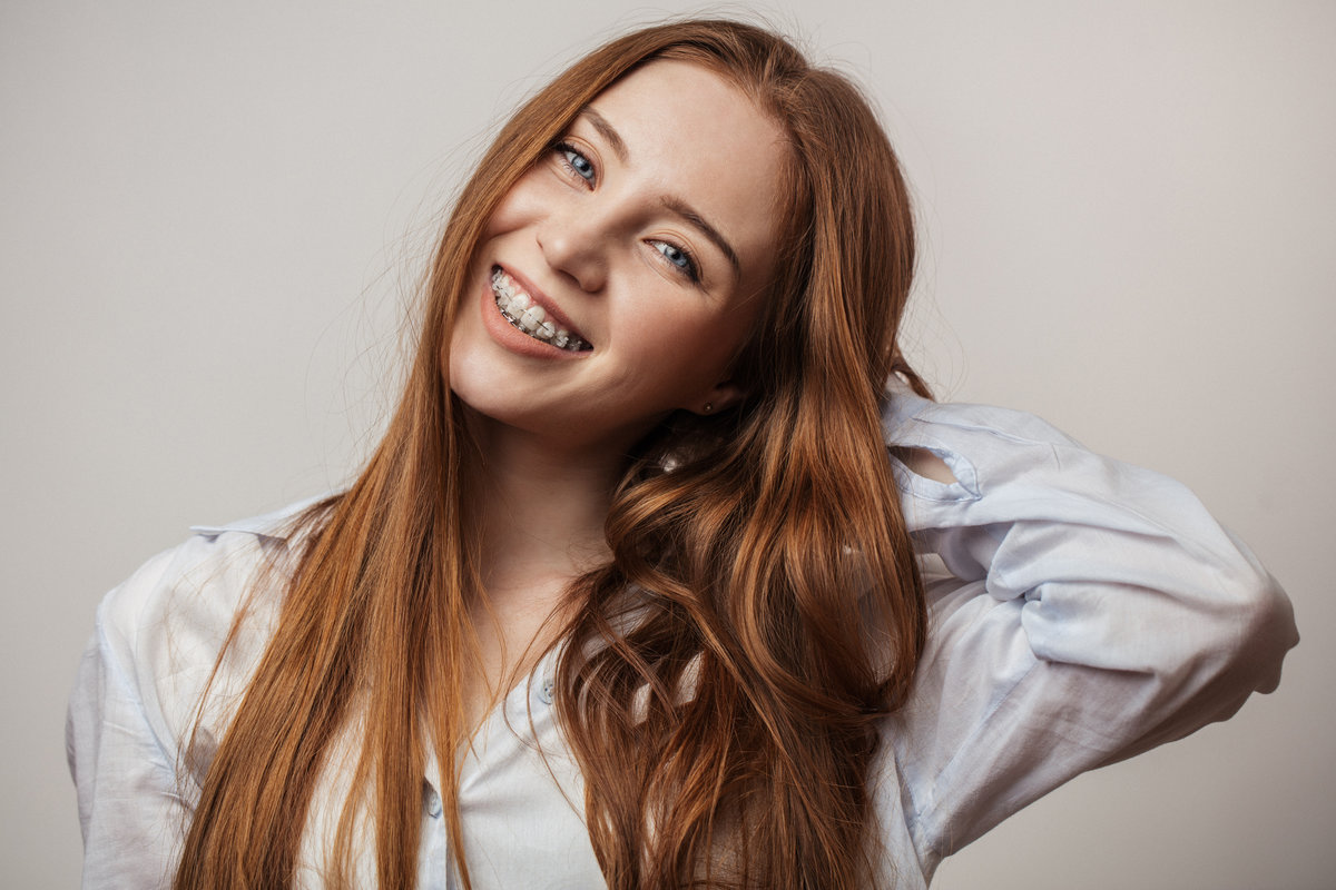 Happy young red-haired woman in braces smiling on white backgrou Airways and Orthodontics