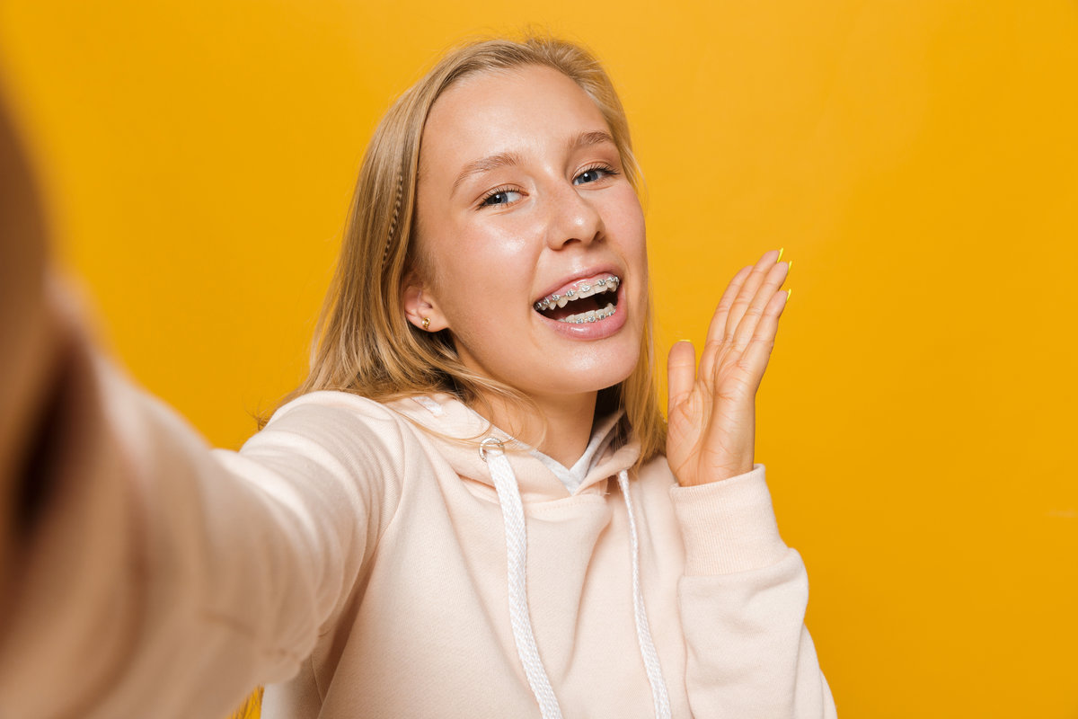 Photo of cheerful girl 16-18 with dental braces smiling and taking selfie, isolated over yellow background Photo of cheerful girl 16-18 with dental braces smiling and taking selfie isolated over yellow background