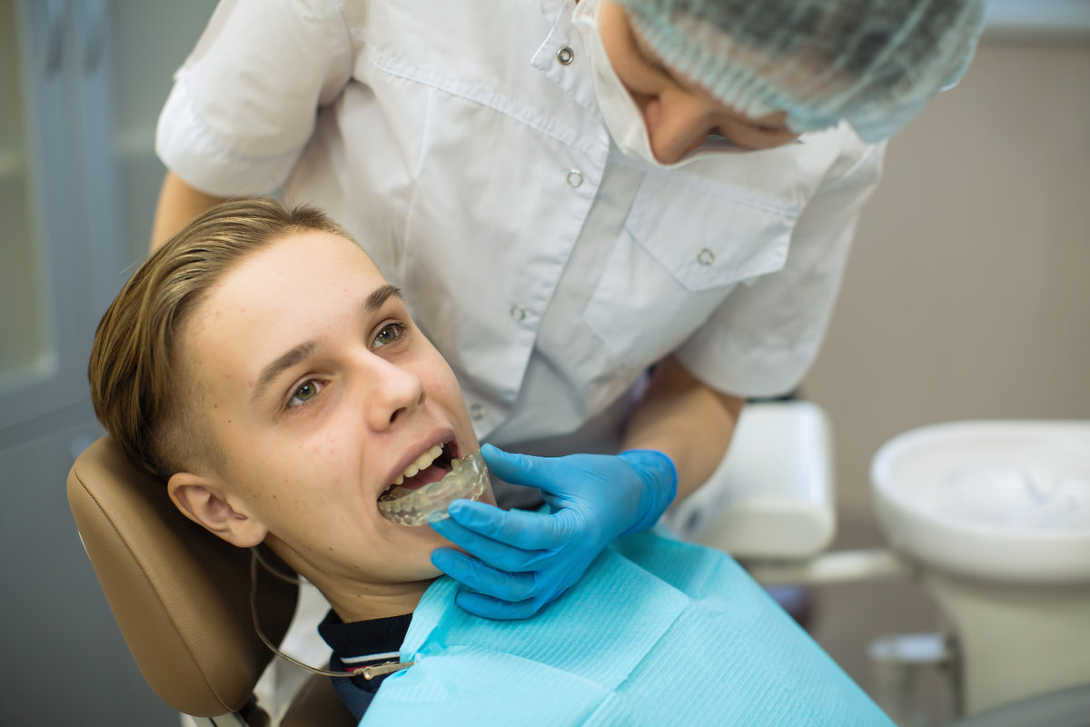 Female dentist puts on a guy patient a mouth guard (a removable orthodontic teeth alignment and correction trainer appliance) in dental office. Female dentist puts on a guy patient a mouth guard (a removable orthodontic teeth alignment and correction trainer appliance) in dental office.
