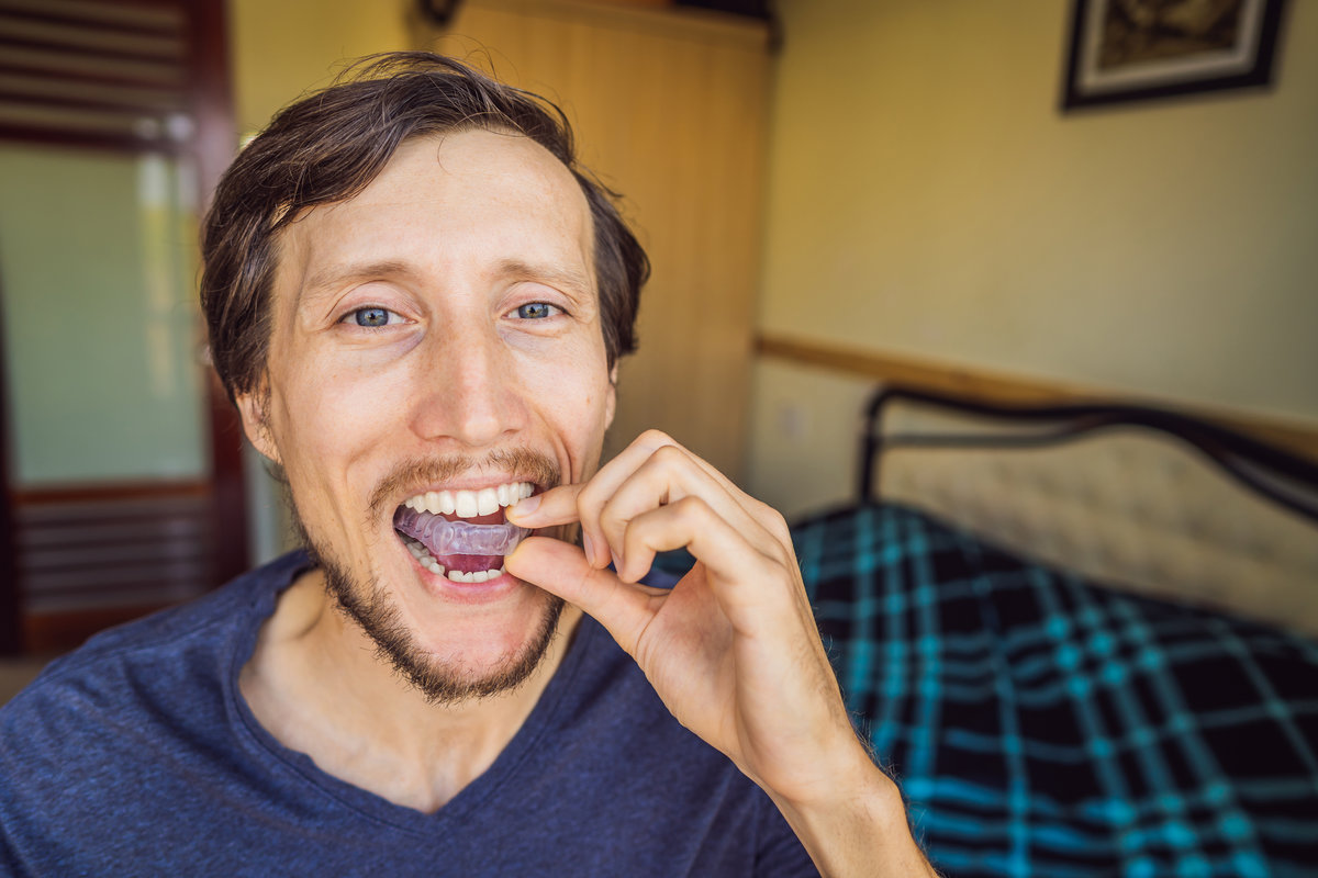 Man placing a bite plate in his mouth to protect his teeth at night from grinding caused by bruxism, close up view of his hand and the appliance Airways and Orthodontics