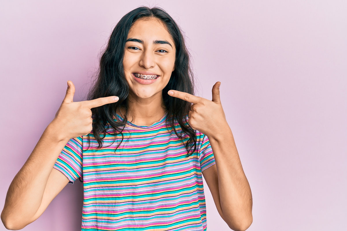 Hispanic teenager girl with dental braces wearing casual clothes smiling cheerful showing and pointing with fingers teeth and mouth. dental health concept. Hispanic teenager girl with dental braces wearing casual clothes smiling cheerful showing and pointing with fingers teeth and mouth. dental health concept.