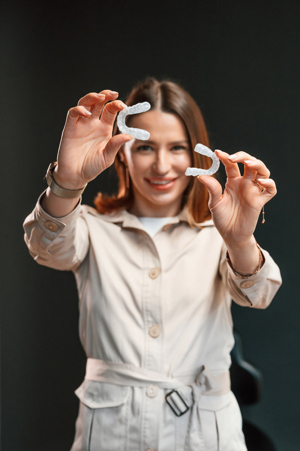 Holding two aligners. Young woman is standing against black background and holding.