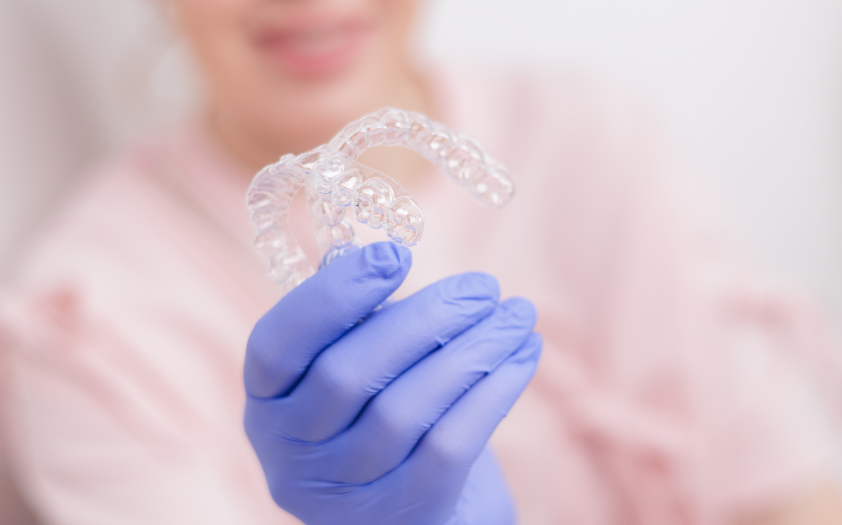 Dentist holding clear retainers in blue gloved hand, orthodontic appliance to make teeth straight.