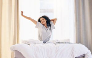 Morning stretching, black woman and wake up in home bedroom after sleeping or resting. Relax, peace and comfort of happy female stretch after sleep feeling fresh, awake and well rested in house