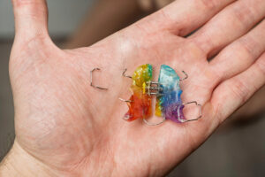 Male hand holding broken colorful orthodontic plate for child, small metal piece lying aside, concept of dental repair and care
