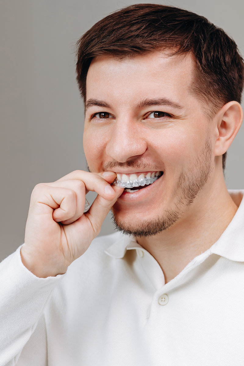 Young man inserting clear aligner tray for teeth, dental care and confident smile at home Young man inserts a clear aligner tray while smiling, demonstrating at-home orthodontic care, dental hygiene and confident oral health. Casual close-up portrait in a white shirt for lifestyle and self-care.
