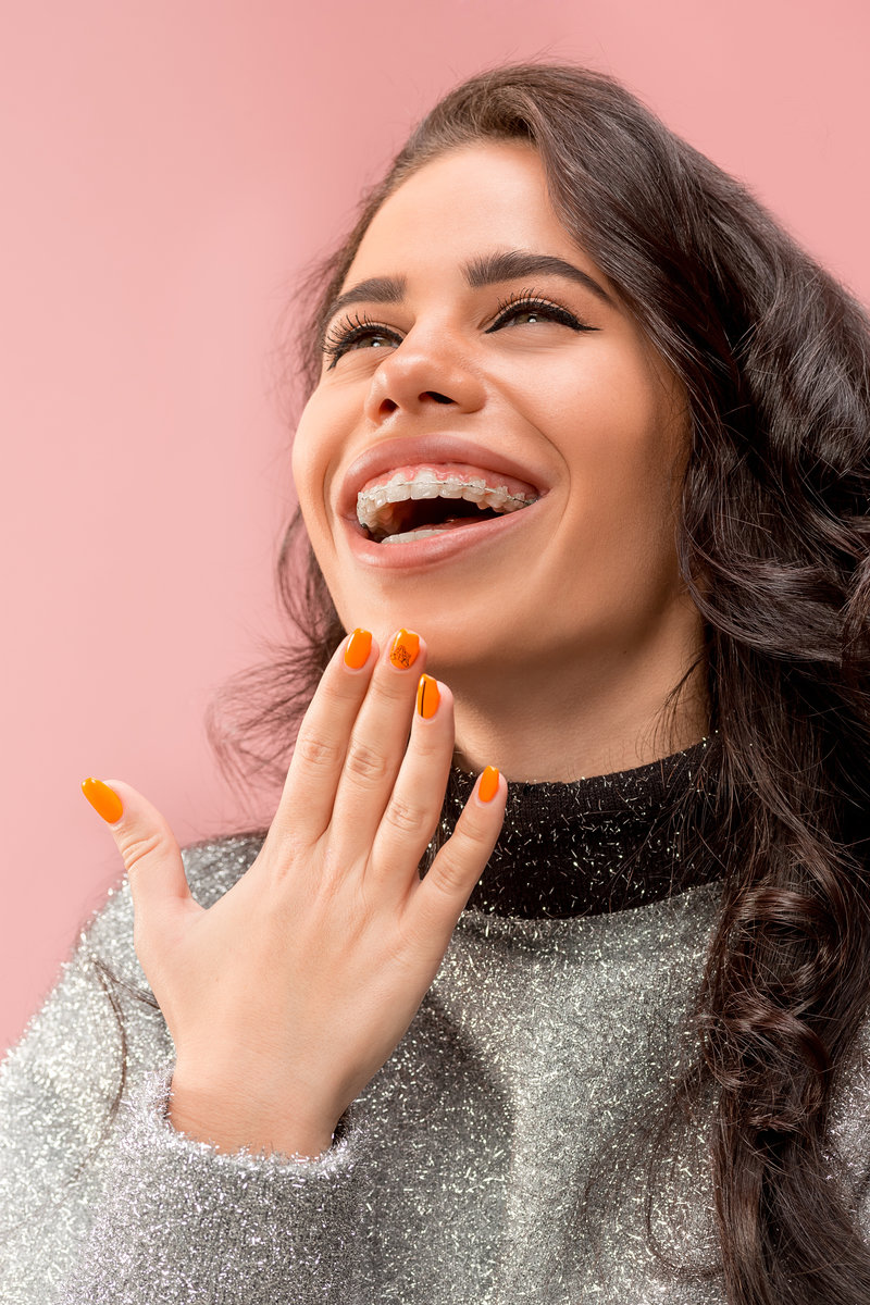 Beautiful young woman with teeth braces on pink