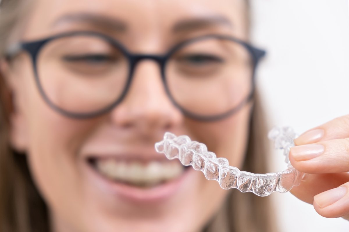 Smiling woman holding a clear Invisalign aligner tray