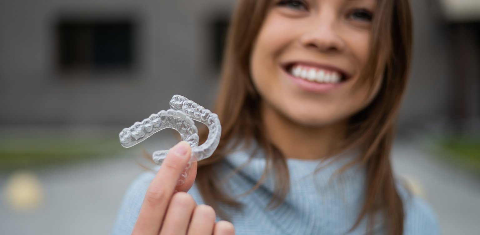 Woman with a healthy smile holding a clear removable retainer